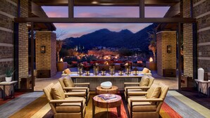A modern outdoor seating area with leather chairs and a central table, overlooking a mountainous landscape at dusk.