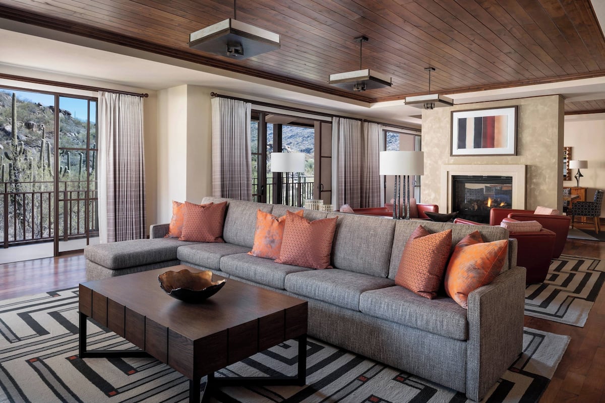 A modern living room with a sectional sofa, a fireplace, and large windows offering a view of the outdoors.