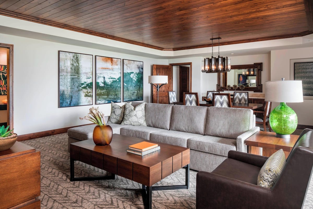 A modern living room with a wooden ceiling, a grey sofa, a wooden coffee table, and a green vase.