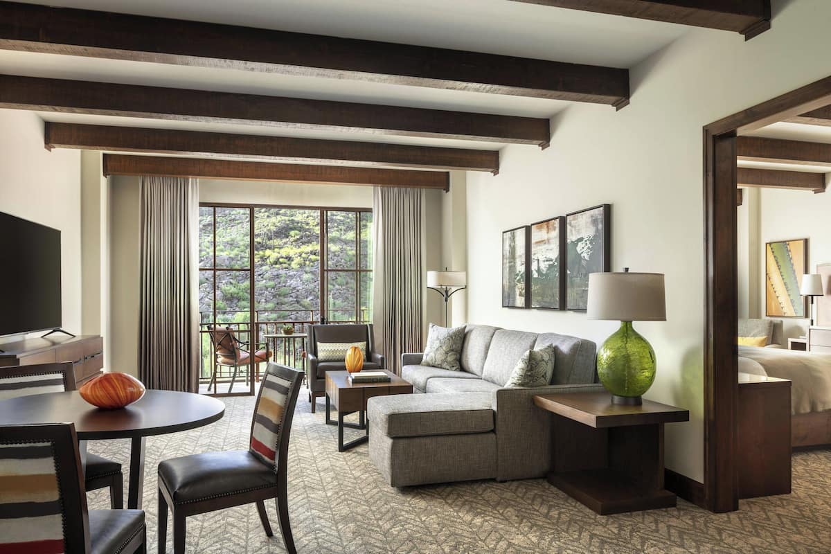 A hotel room with a sofa, armchair, dining table, and a TV.