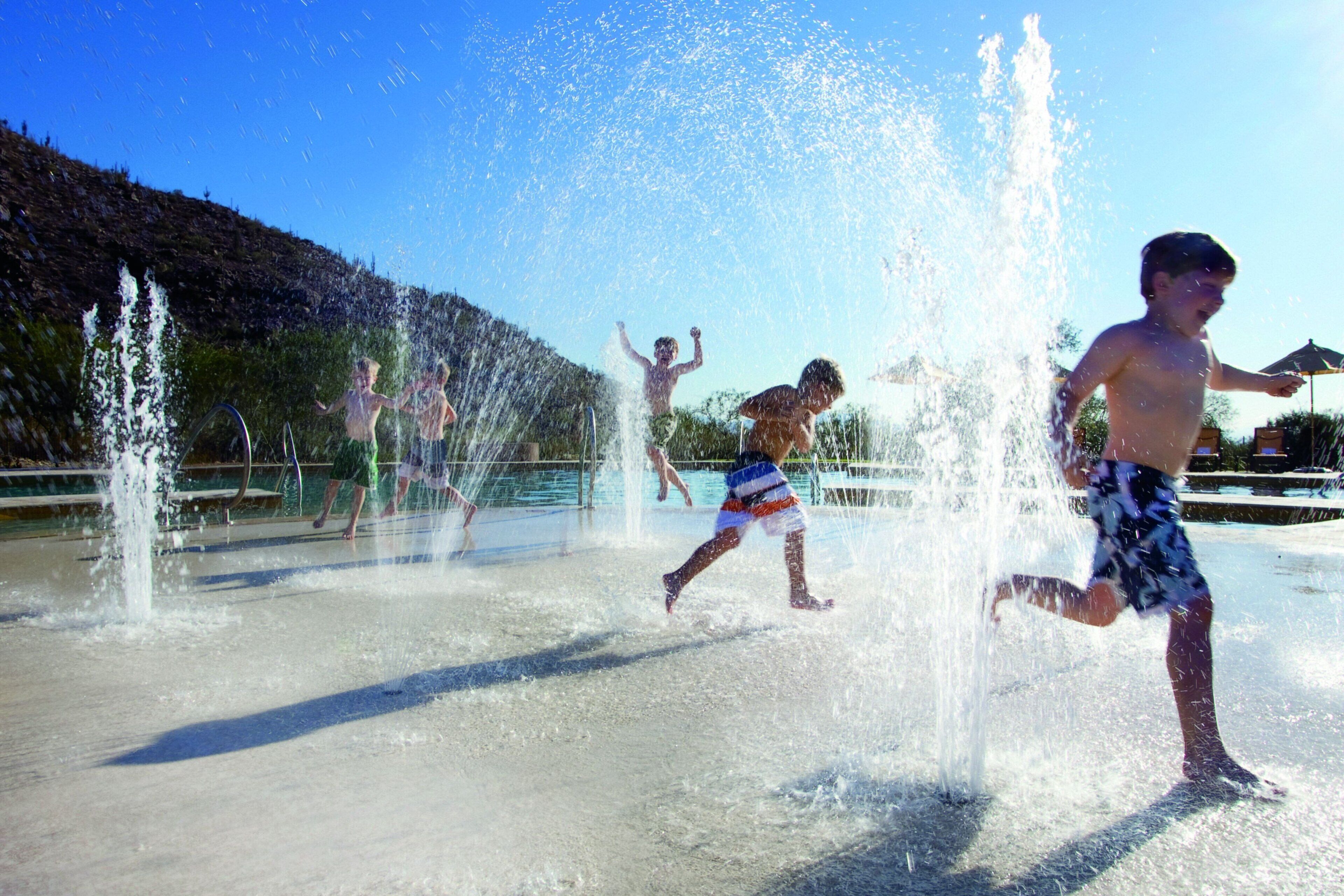 A water play area with multiple water jets and a hilly landscape in the background.