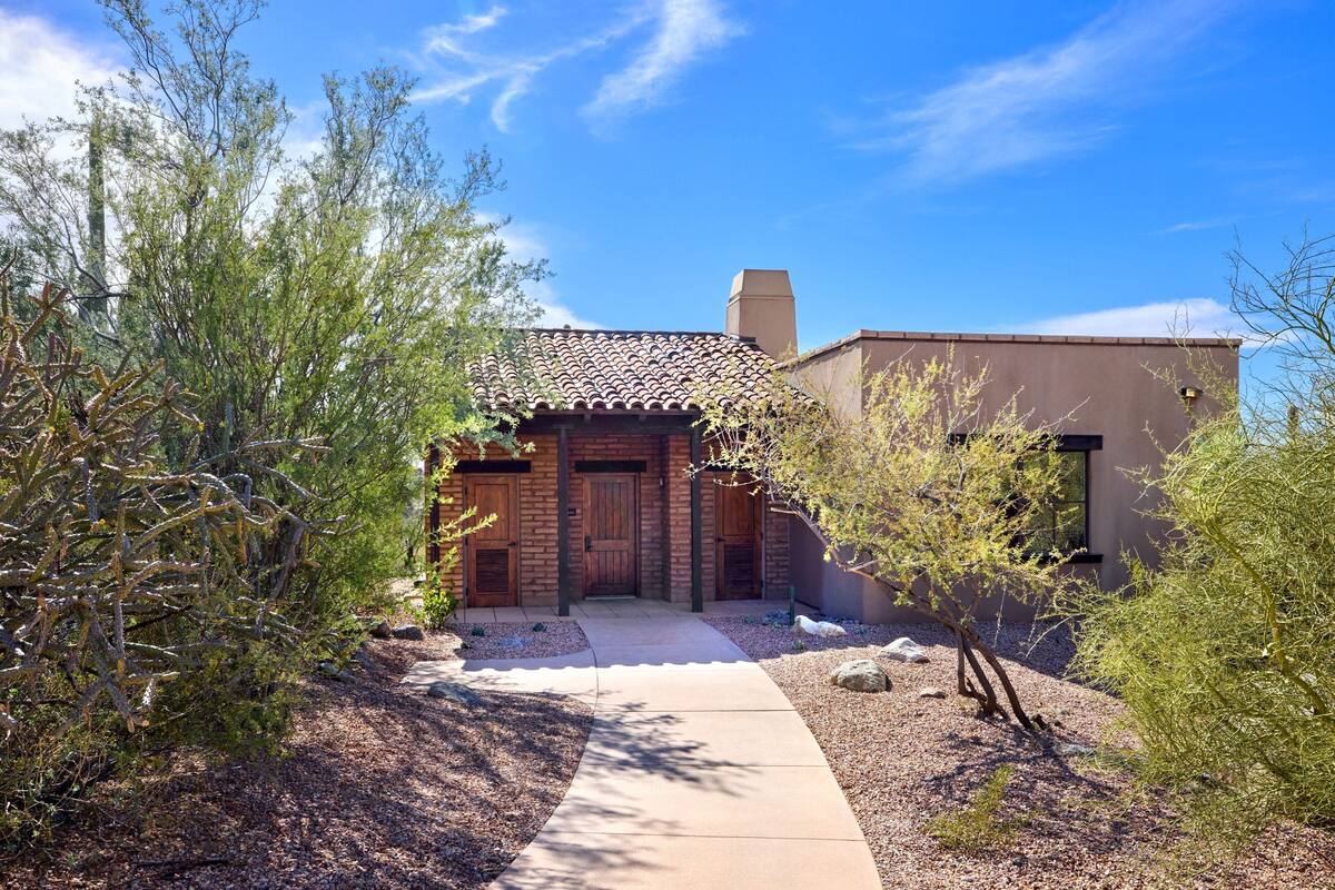 A rustic building with a brick facade and a tiled roof, surrounded by desert vegetation.
