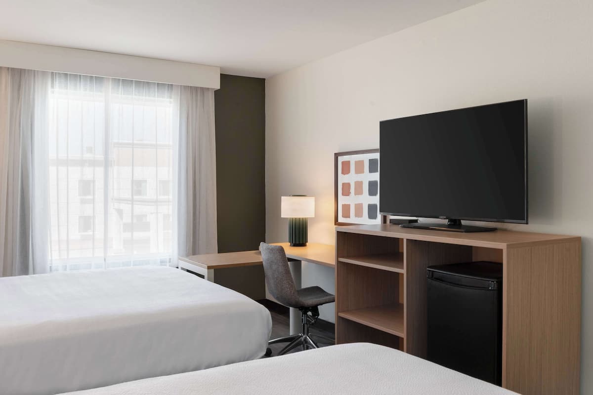 Habitación de hotel con dos camas, un escritorio con lámpara, televisión y refrigerador pequeño.