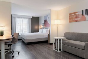 Une chambre d’hôtel avec un lit, un bureau, une chaise, un canapé et une lampe.