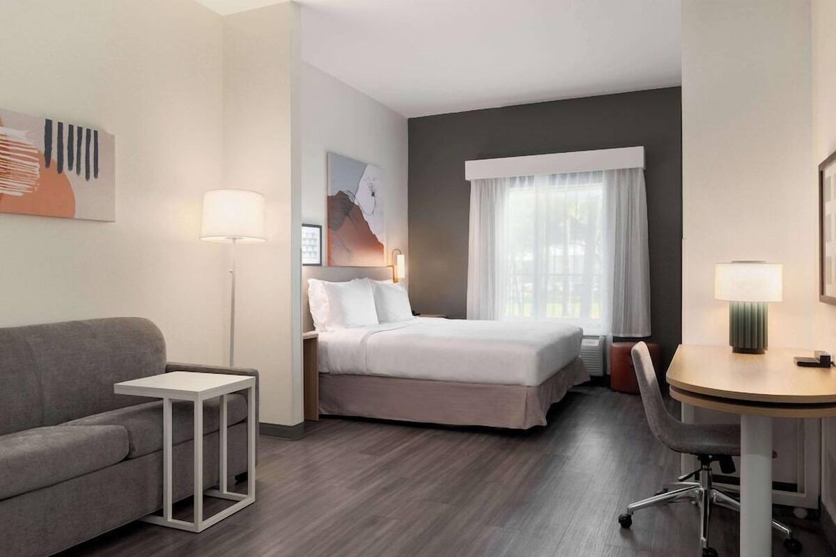 Una habitación de hotel con cama, escritorio, sillón, sofá, lámpara y obras de arte en las paredes.