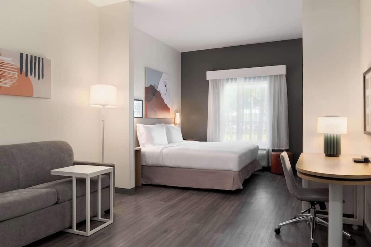 Una habitación de hotel con cama, escritorio, sillón, sofá, lámpara y obras de arte en las paredes.