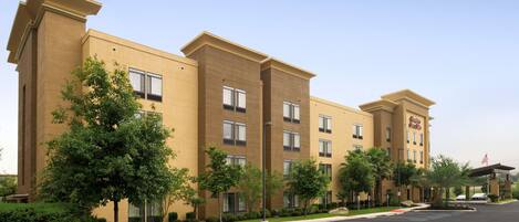 A multi-story hotel with a beige facade, multiple windows, and a parking lot in front.