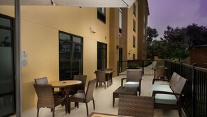 Un espacio de patio al aire libre con mobiliario de mimbre, una mesa de vidrio y una zona de estar cubierta.