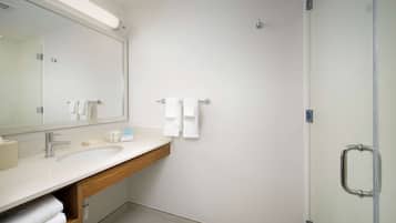 A modern bathroom with a large mirror, white sink, and a glass shower enclosure.