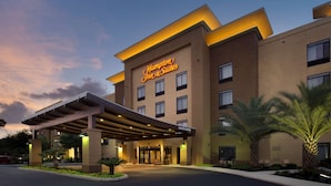 Un hotel Hampton Inn & Suites con una fachada moderna, un acceso cubierto y palmeras en el paisajismo.