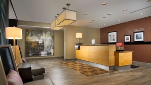 Zona de recepción de un hotel con un mostrador de madera, un cuadro abstracto grande y un escritorio con lámpara.