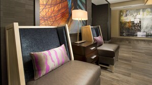 Un moderno vestíbulo de hotel con un área de descanso que incluye un sofá, sillones, una lámpara de pie y un cuadro abstracto grande en la pared.