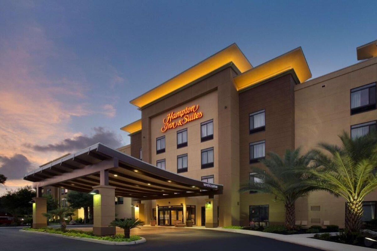 Edificio de Hampton Inn & Suites con entrada cubierta, varios pisos y un cartel acogedor.