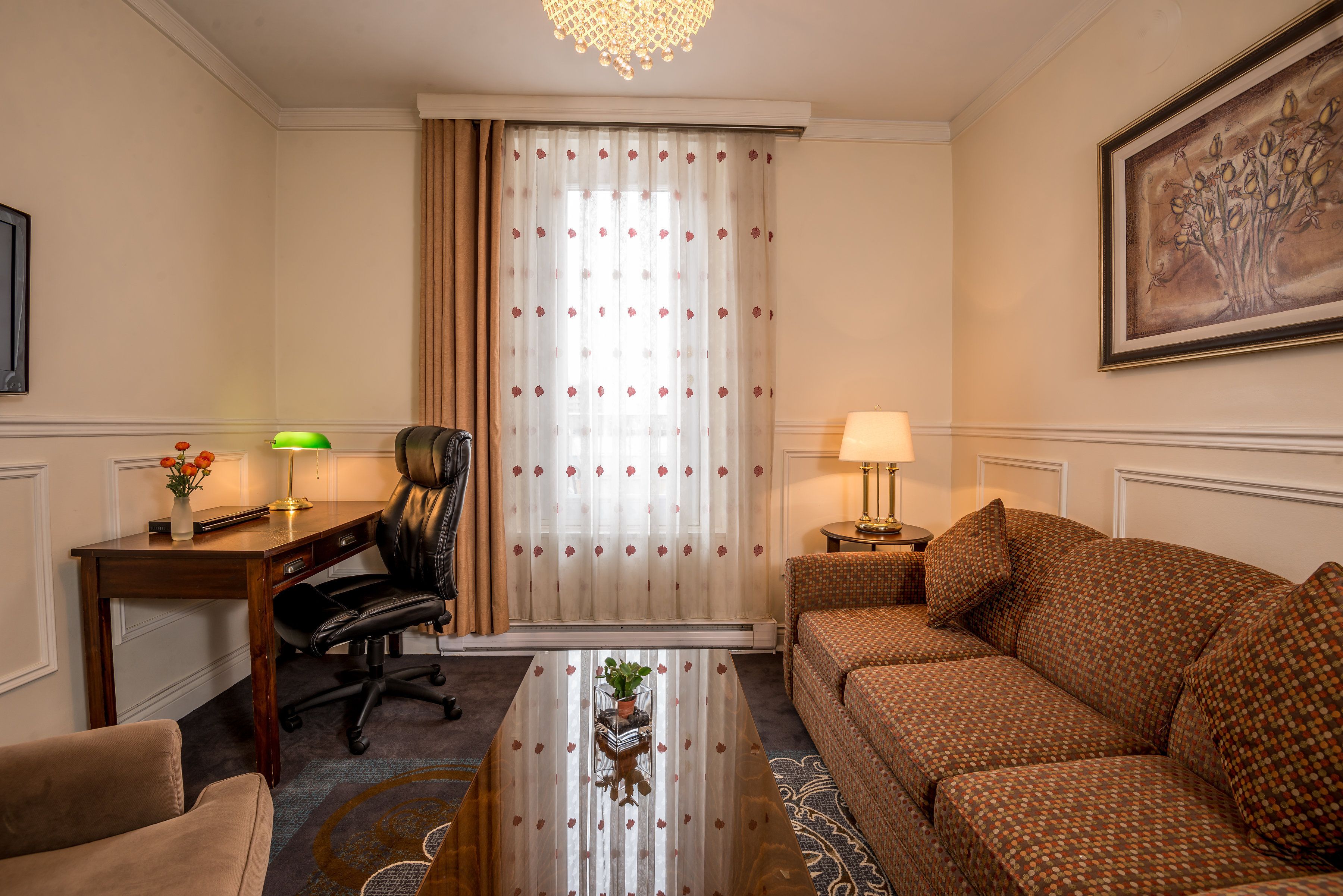 Une chambre d’hôtel avec un bureau en bois, un fauteuil en cuir, un canapé, une table basse et un tableau au mur.