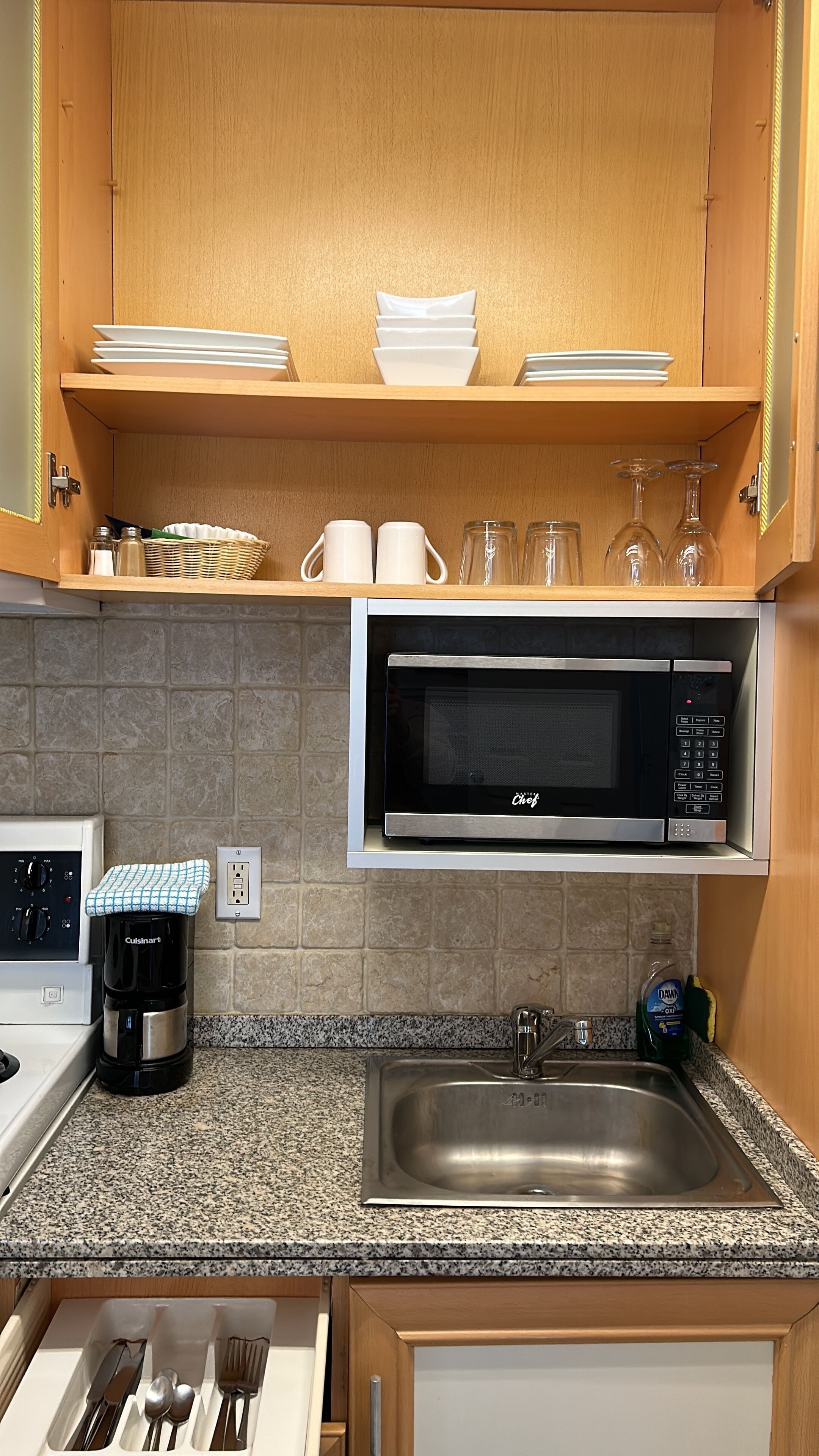 Una cocina con armarios de madera, un lavamanos de acero inoxidable, una cafetera Cuisinart, un microondas y una encimera de granito.