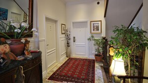 A hallway with a red patterned rug, white doors, a mirror, and a potted plant. - Parc Suites Hotel (Montreal)