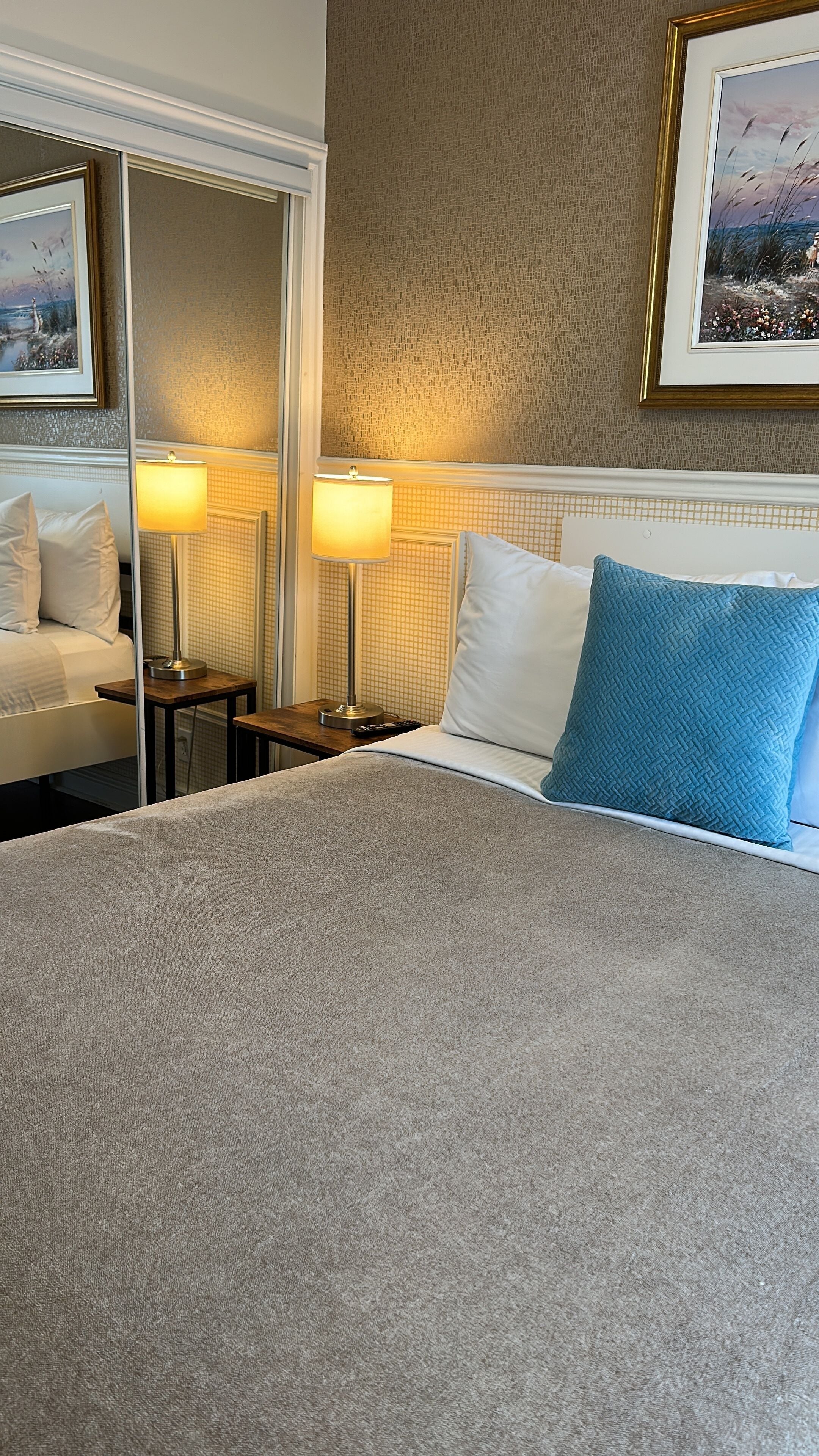 A hotel room with a large bed, two bedside tables with lamps, a mirror, and a framed picture on the wall.