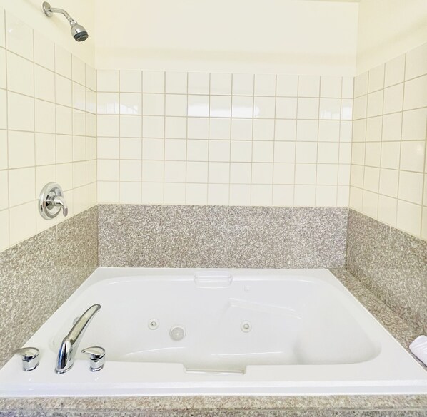 A rectangular bathtub with a chrome faucet and a handheld showerhead, set against a tiled wall with a granite countertop.