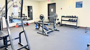 Une salle de sport équipée de matériel d’exercice, de supports pour les poids et d’une porte marquée « SORTIE ».