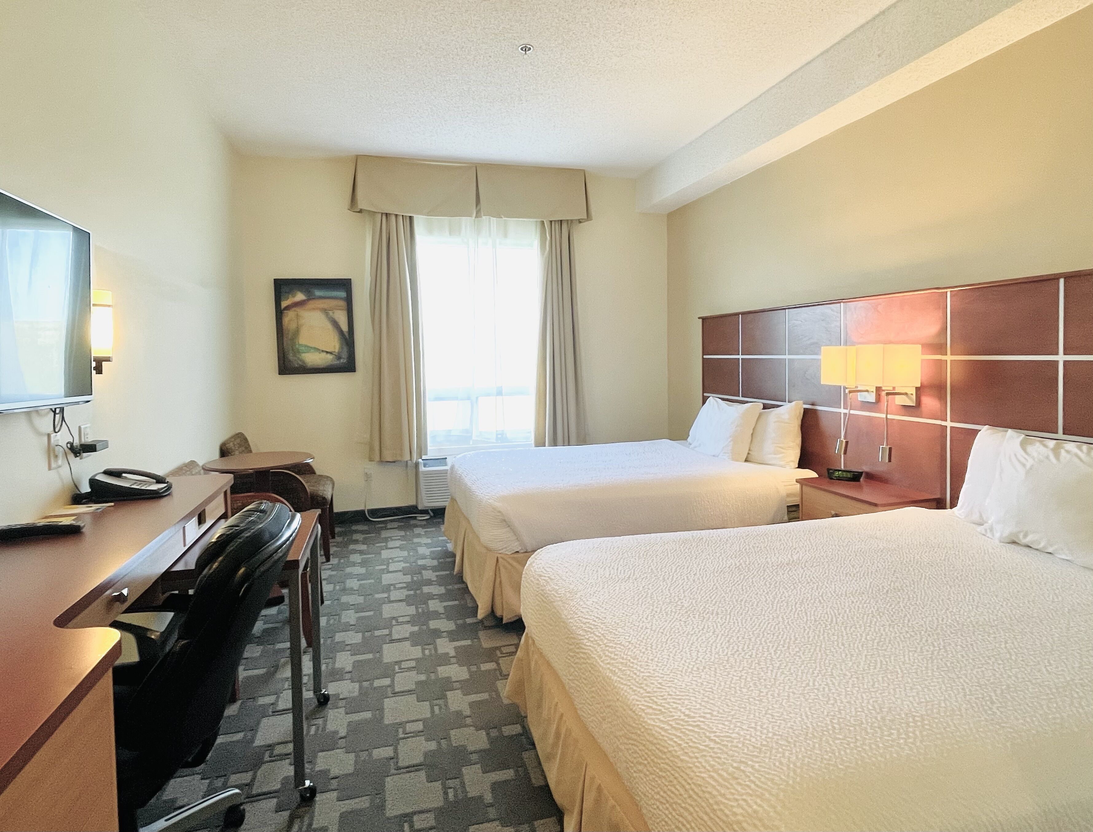 Une chambre d’hôtel avec deux lits, un bureau avec un téléphone, une télévision et une fenêtre avec des rideaux.
