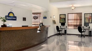 Un espace d’accueil avec un comptoir en granit, une enseigne Days Inn, un bureau de réception et un coin salon avec des chaises et un bureau.