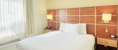 A hotel room with a large bed, two bedside tables with lamps, a telephone, and a window with curtains.