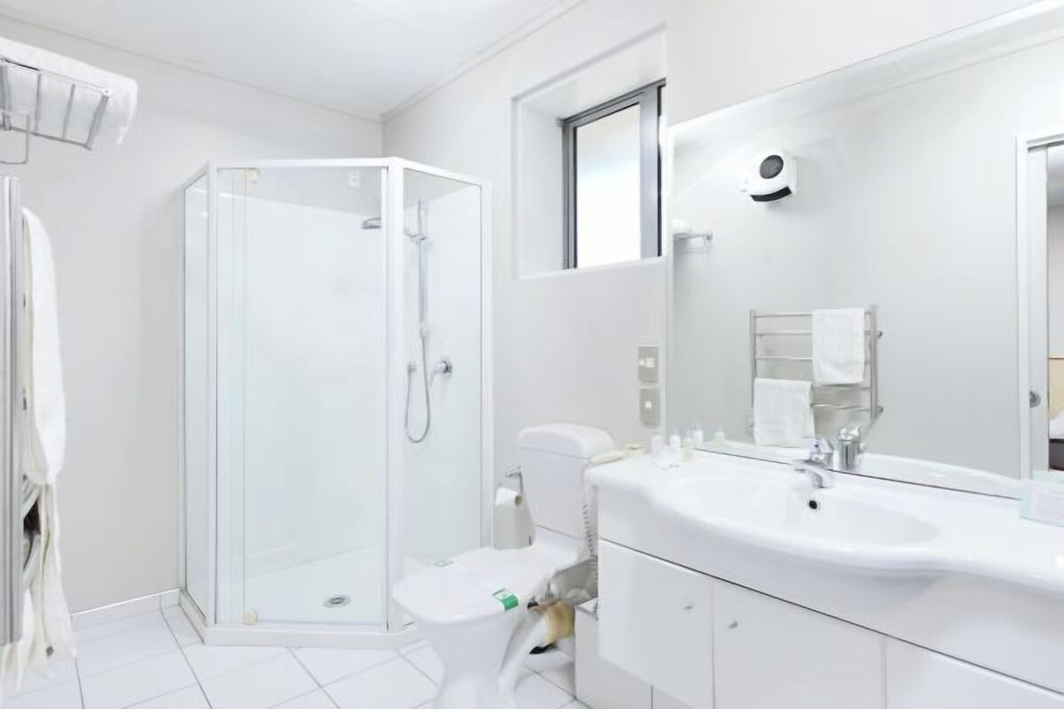Un baño moderno con cabina de ducha de vidrio, un lavabo blanco con espejo y un inodoro.