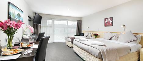 A hotel room with a bed, a desk with a vase of flowers, a TV, and a window with a view of buildings.