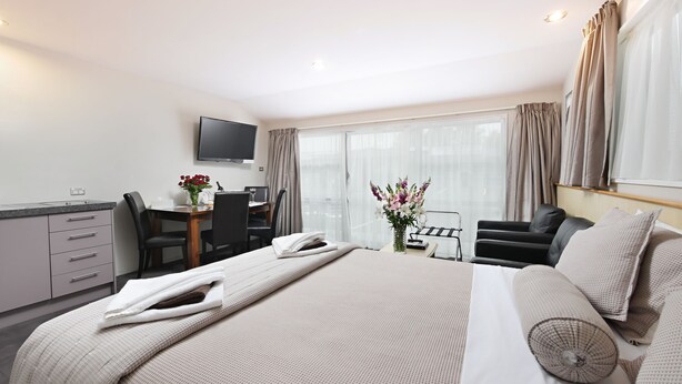 Habitación de hotel con cama, escritorio, silla, televisor y ventana con cortinas.