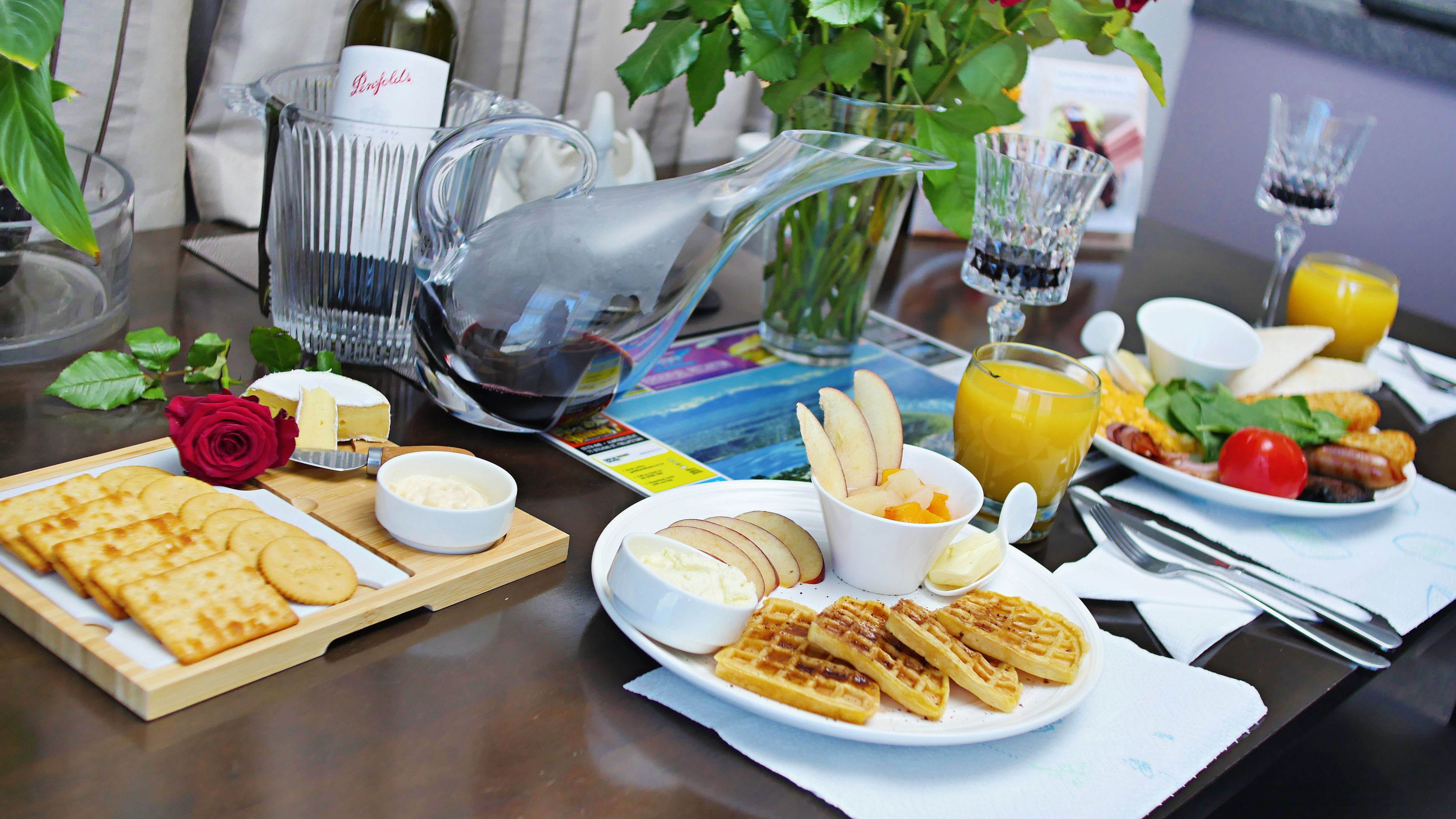 Une table de petit-déjeuner avec des gaufres, du fromage, des fruits et du jus.
