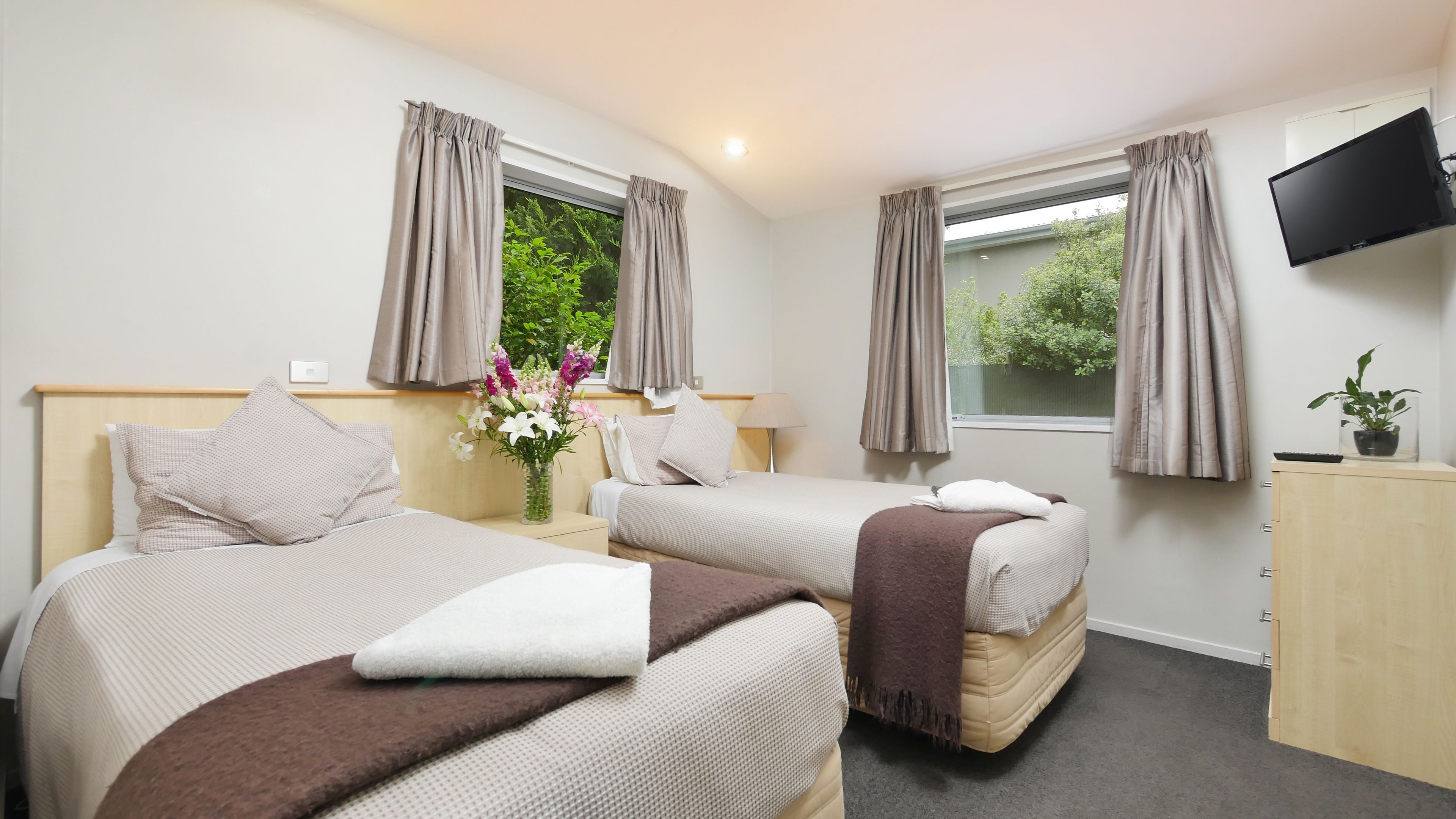 A hotel room with two beds, a TV, a desk, and a window with curtains.