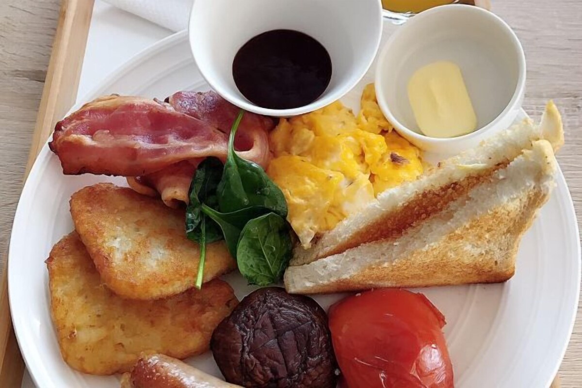 A plate with scrambled eggs, bacon, toast, mushrooms, spinach, and a tomato.