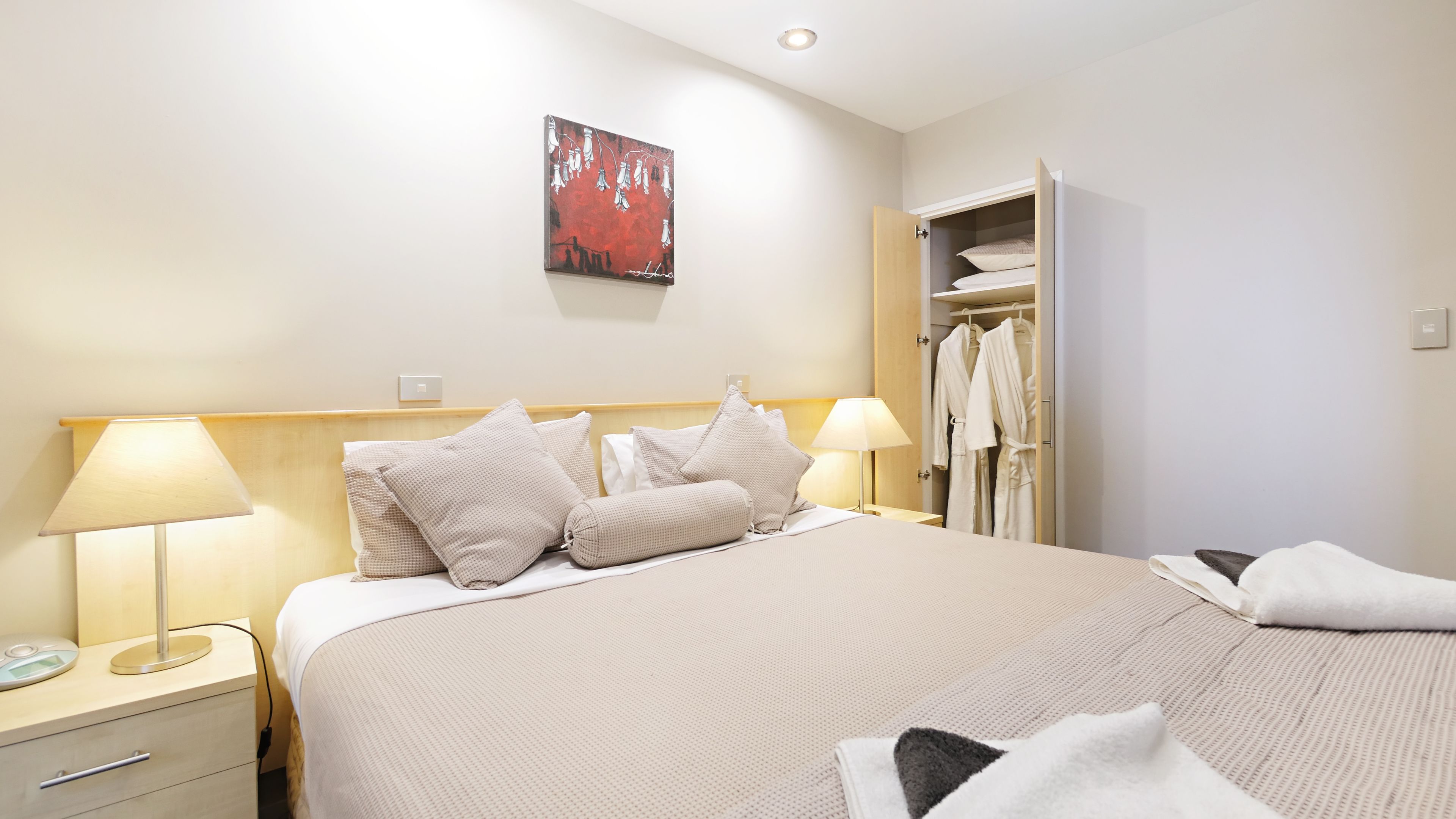 Una habitación de hotel con una cama, dos lámparas de noche, una mesita de noche, un armario y un cuadro en la pared.
