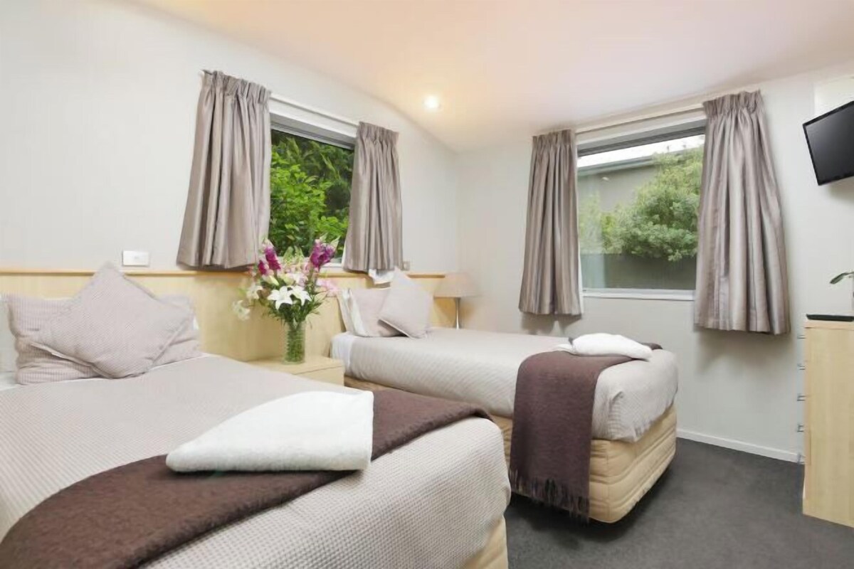 A hotel room with two beds, a TV, a desk, and a window with curtains.