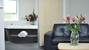 Un baño moderno con un lavamanos blanco, un sofá de cuero negro y un jarrón con flores sobre una mesa de madera.
