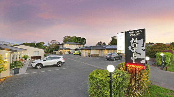 Un motel avec une enseigne indiquant « Arthur’s Court Motel » et une autre indiquant « Complet ». On y voit des voitures garées et une pelouse bien entretenue.