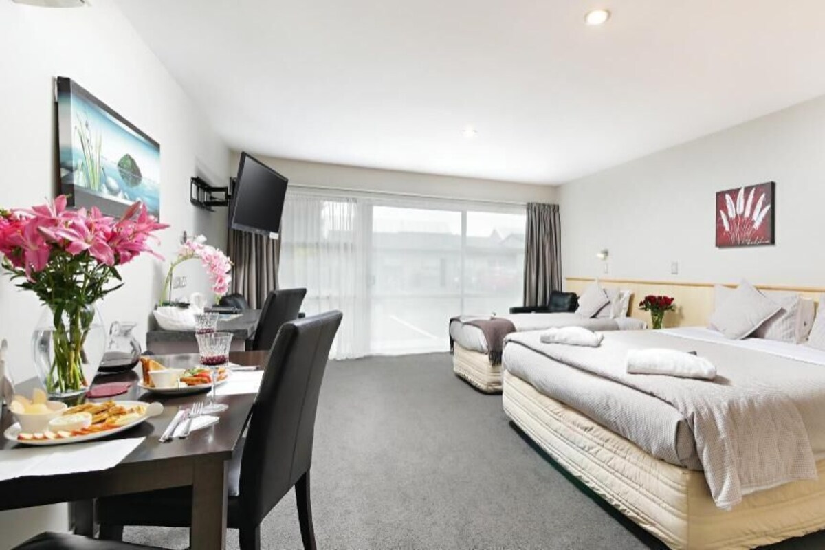 A hotel room with a bed, a desk with a chair, a TV, and a window with curtains.