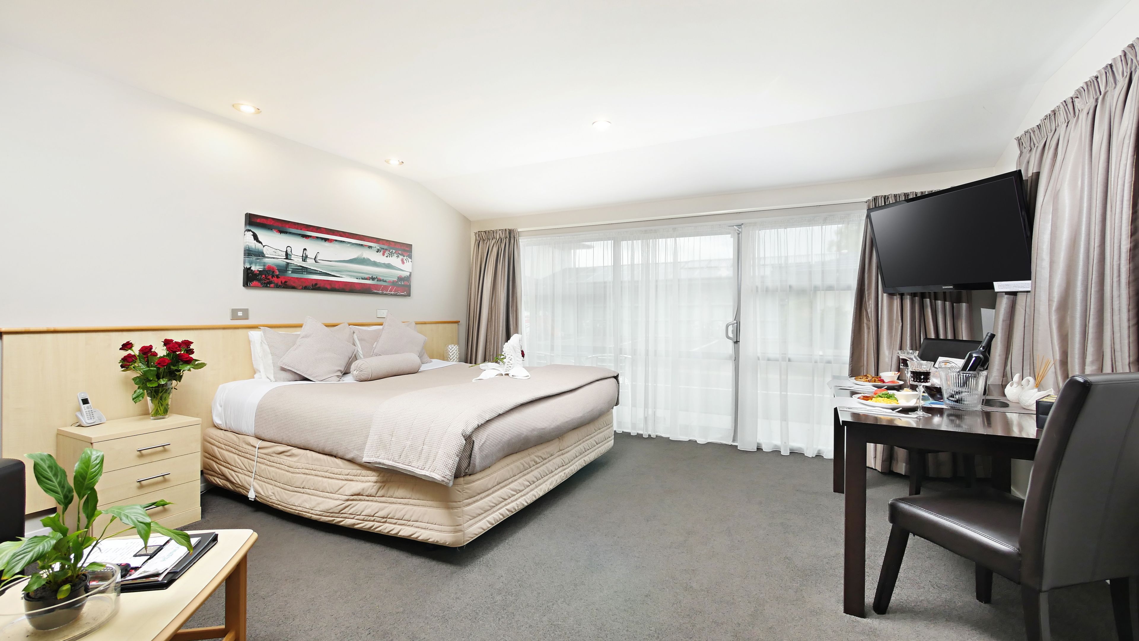 Habitación de hotel con cama, mesita de noche, escritorio, silla, televisor y un cuadro en la pared.