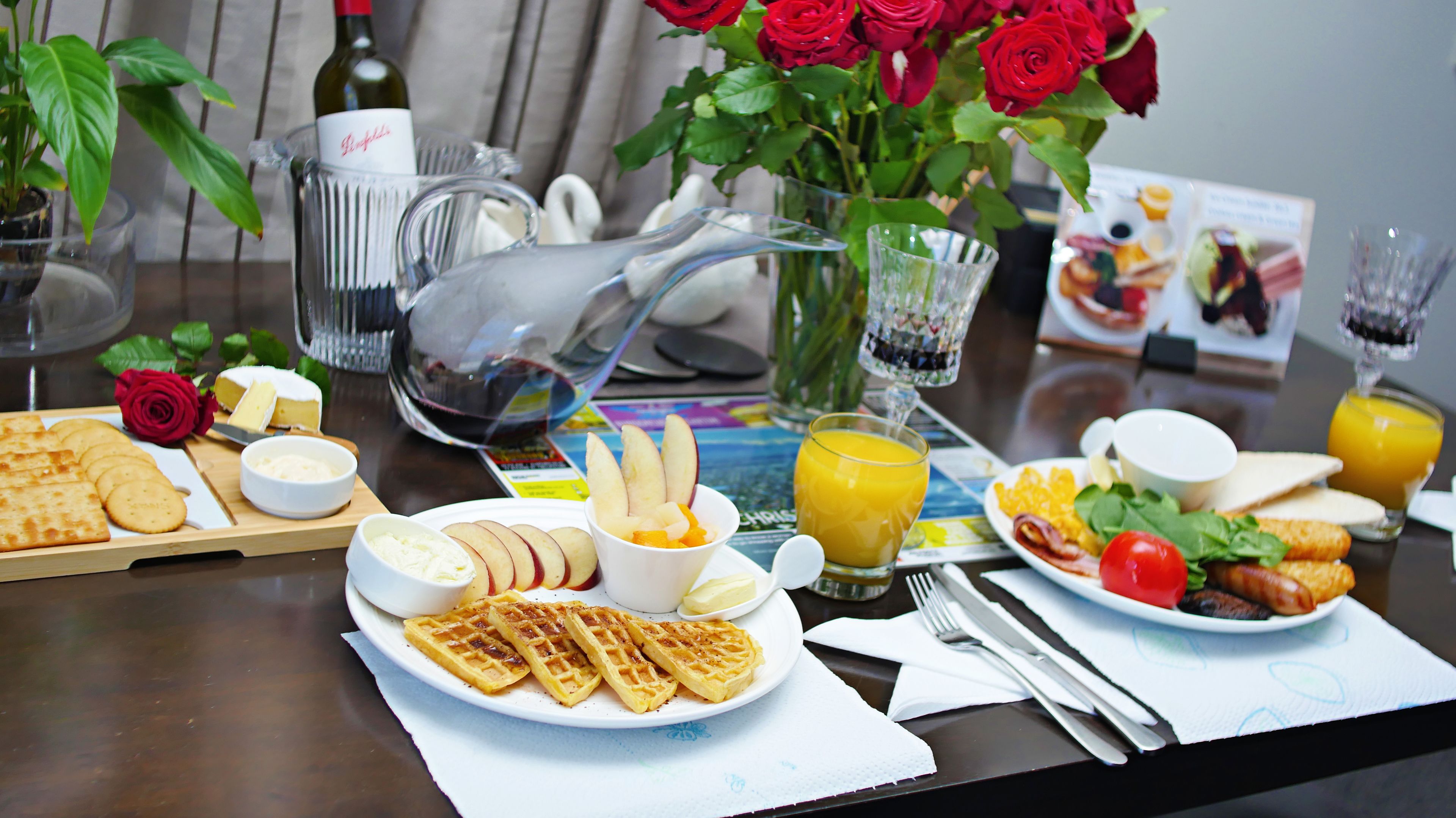 A breakfast table with waffles, fruit, cheese, and a bottle of wine.