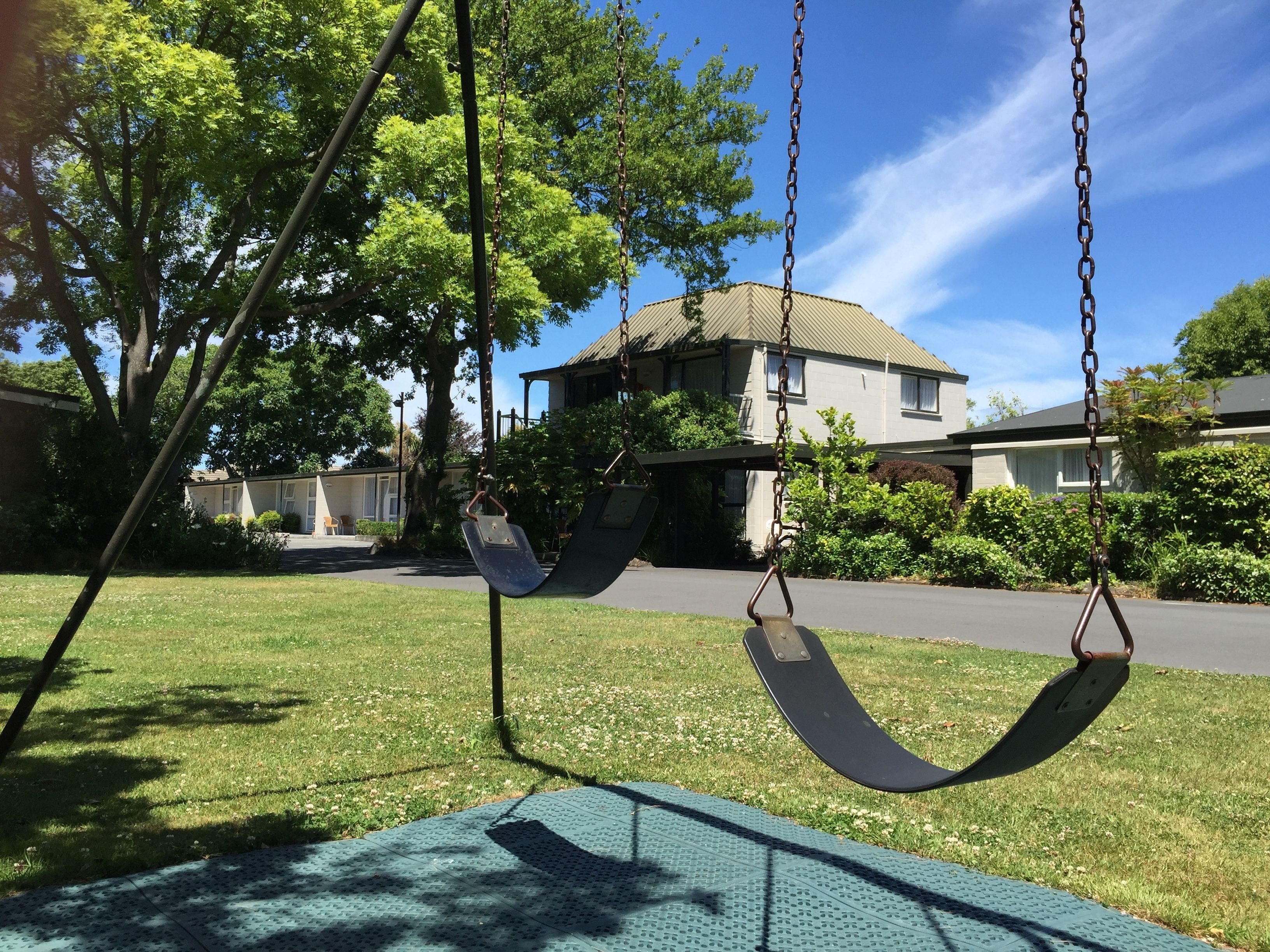 A swing set in a grassy area with a house in the background.
