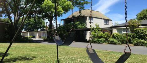A swing set in a grassy area with a house in the background.