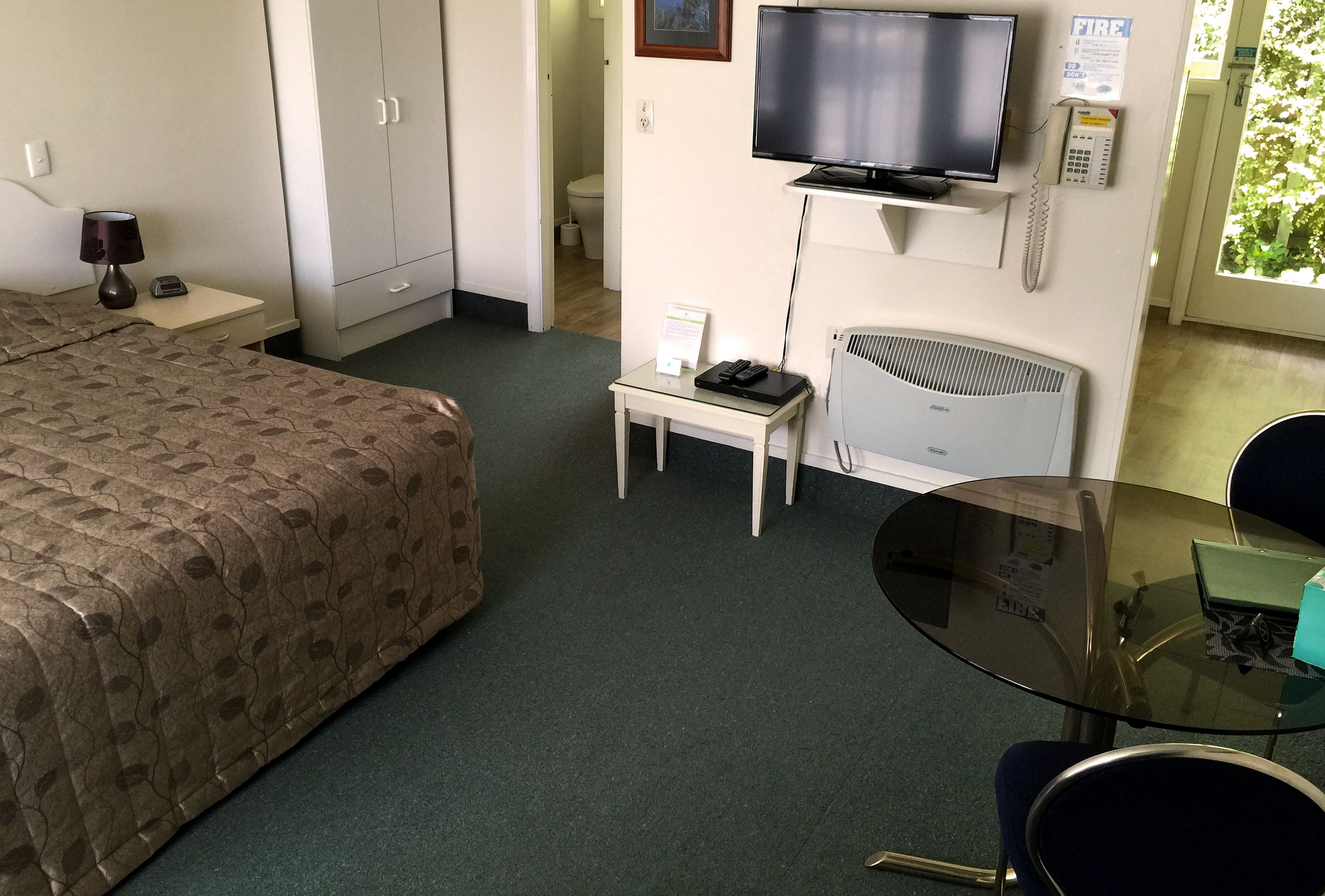 Una habitación de hotel con cama, escritorio con lámpara, televisión, una mesita y una silla.