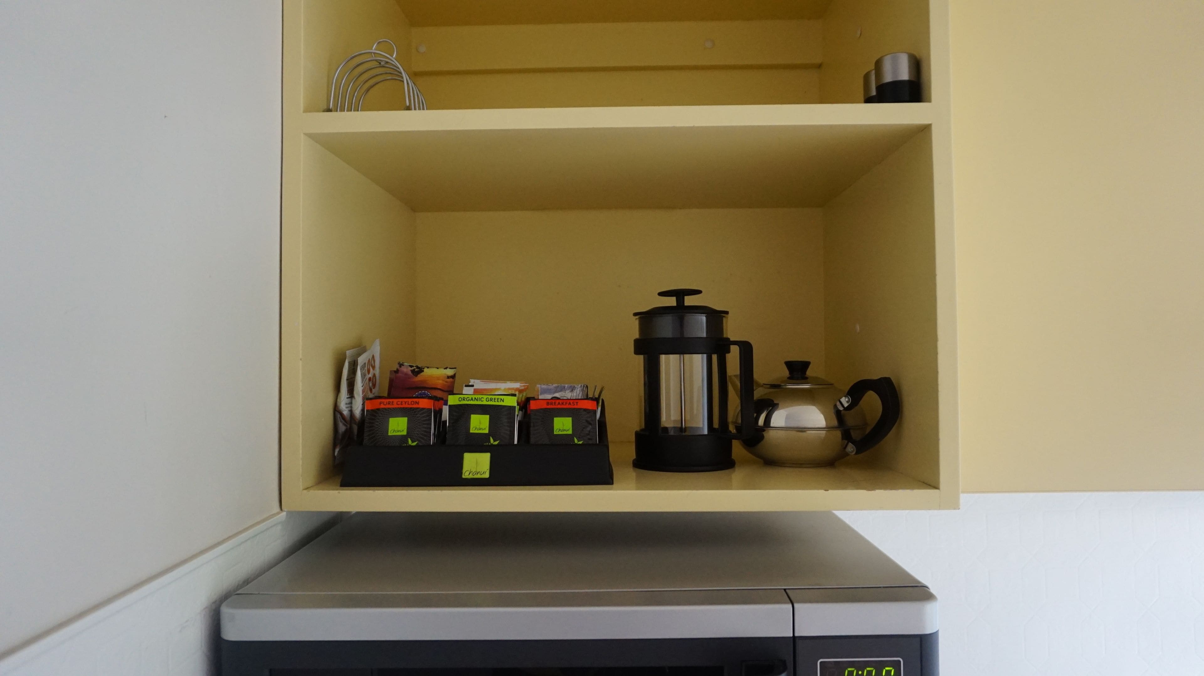 A kitchen shelf with a coffee maker, a kettle, and a coffee grinder.
