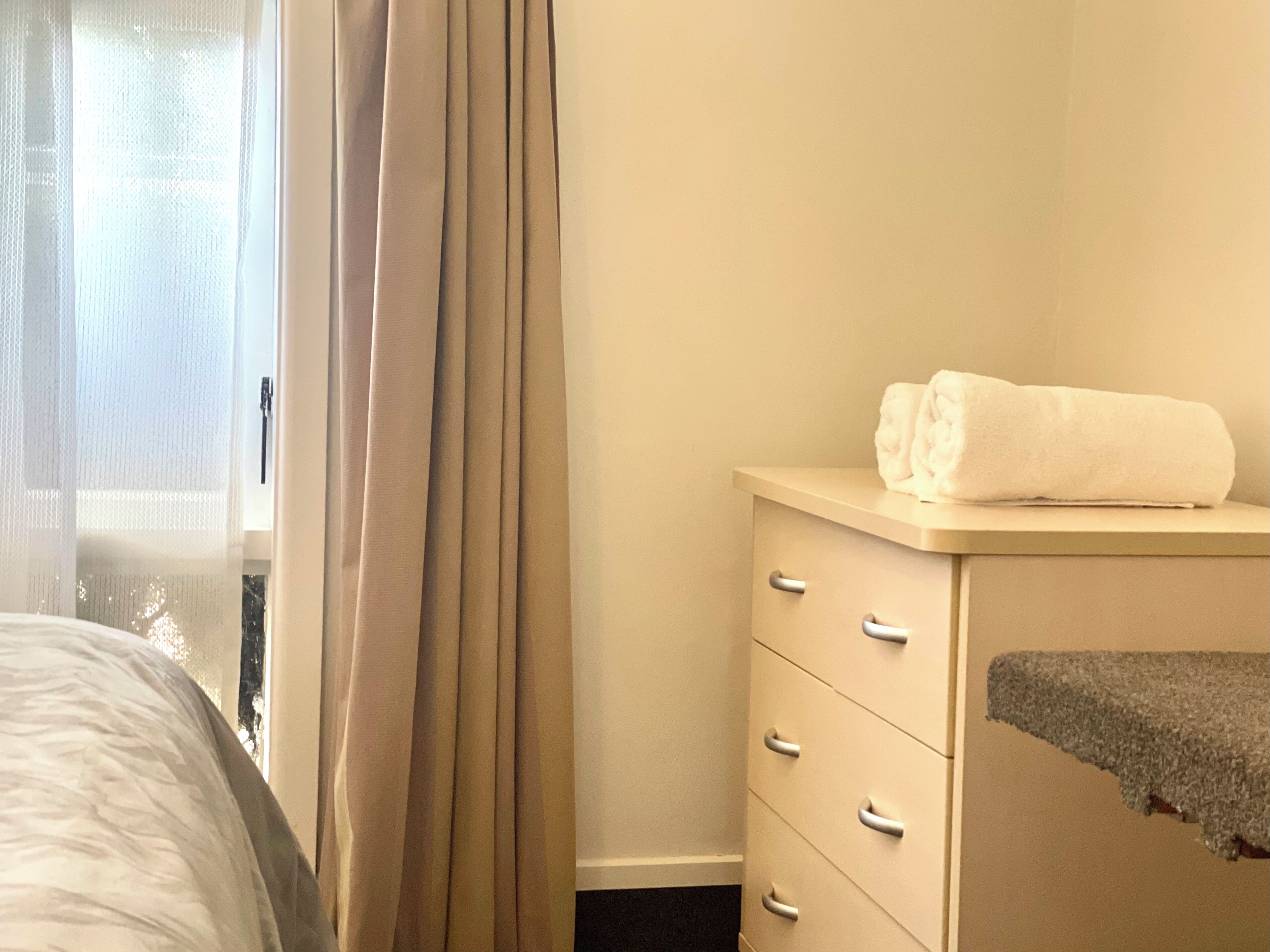 A hotel room with a bed, a dresser, and a window with curtains.
