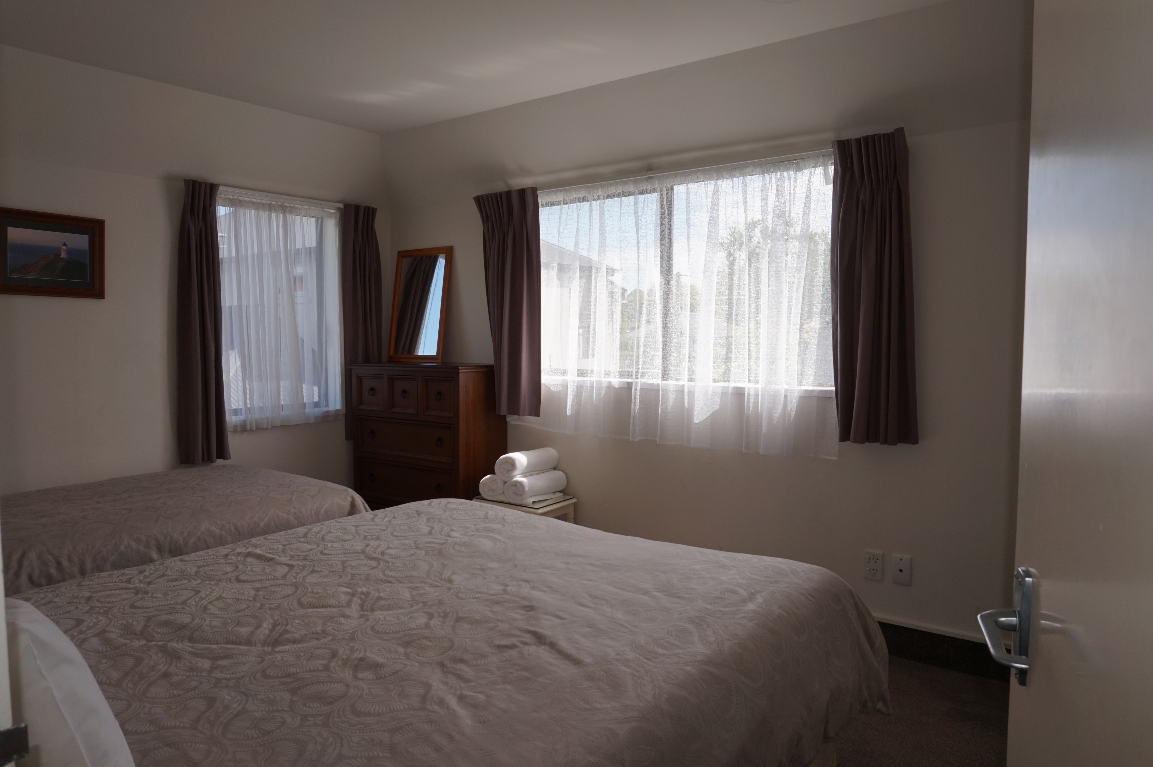Habitación de hotel con dos camas, un aparador, un espejo y una ventana con cortinas.