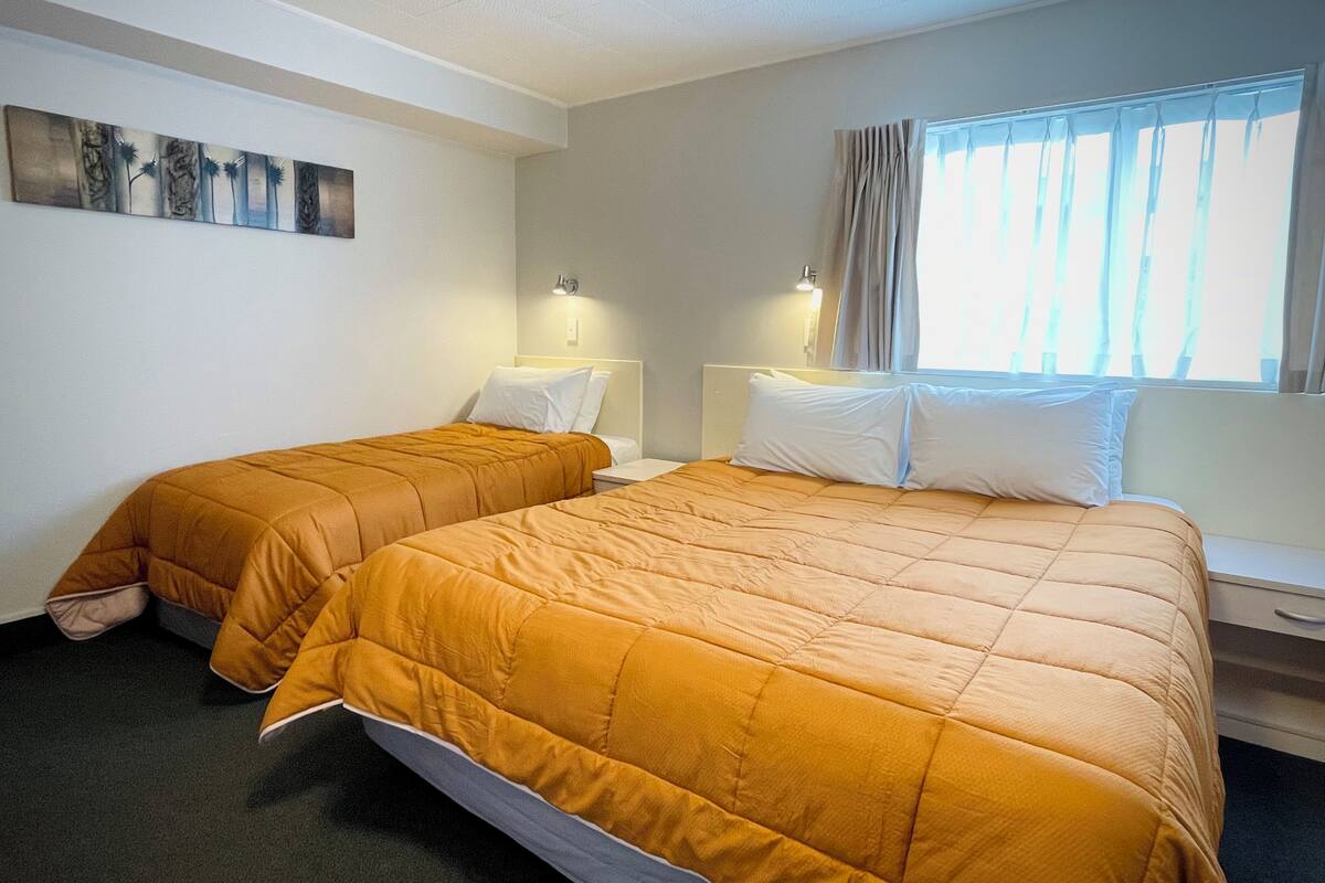 A hotel room with two beds, each with a matching headboard and footboard, and a large window with curtains.