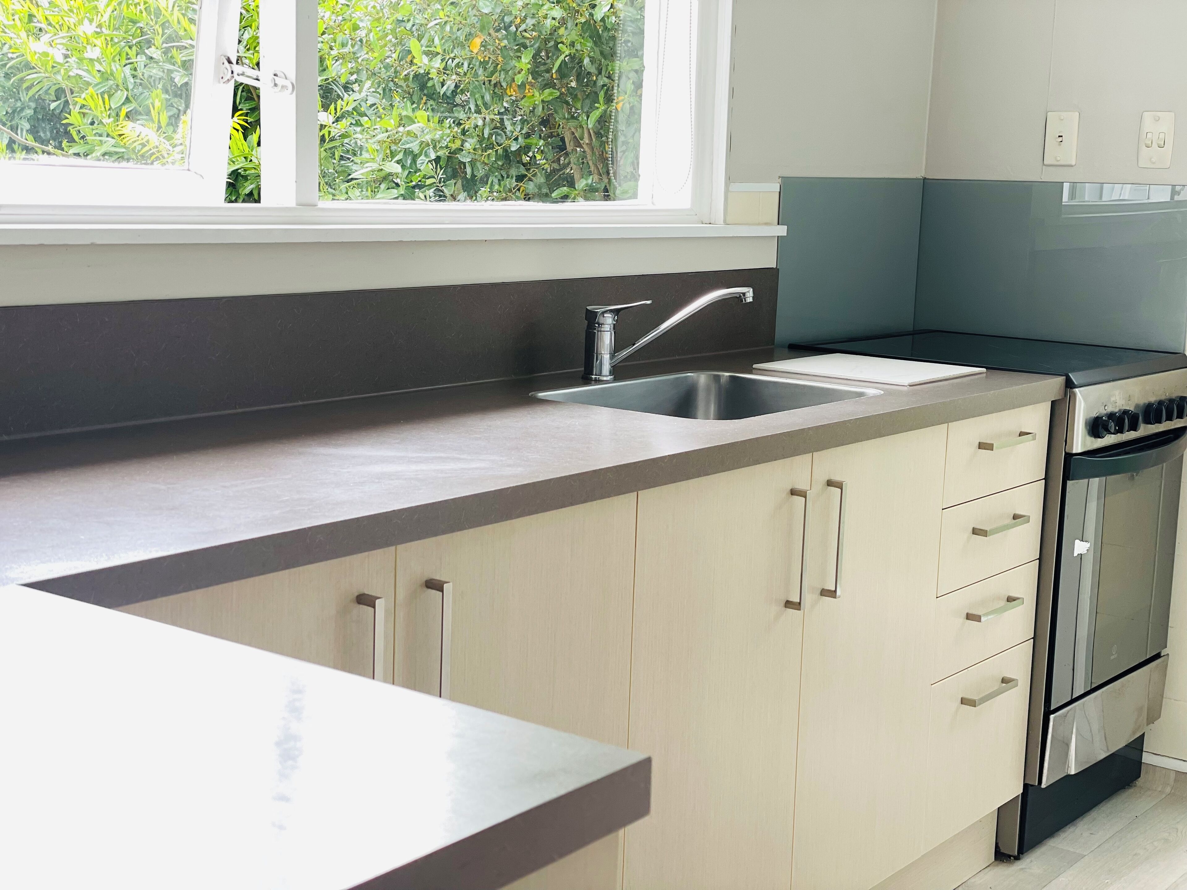A modern kitchen with a stainless steel sink, a built-in oven, and light-colored cabinets.