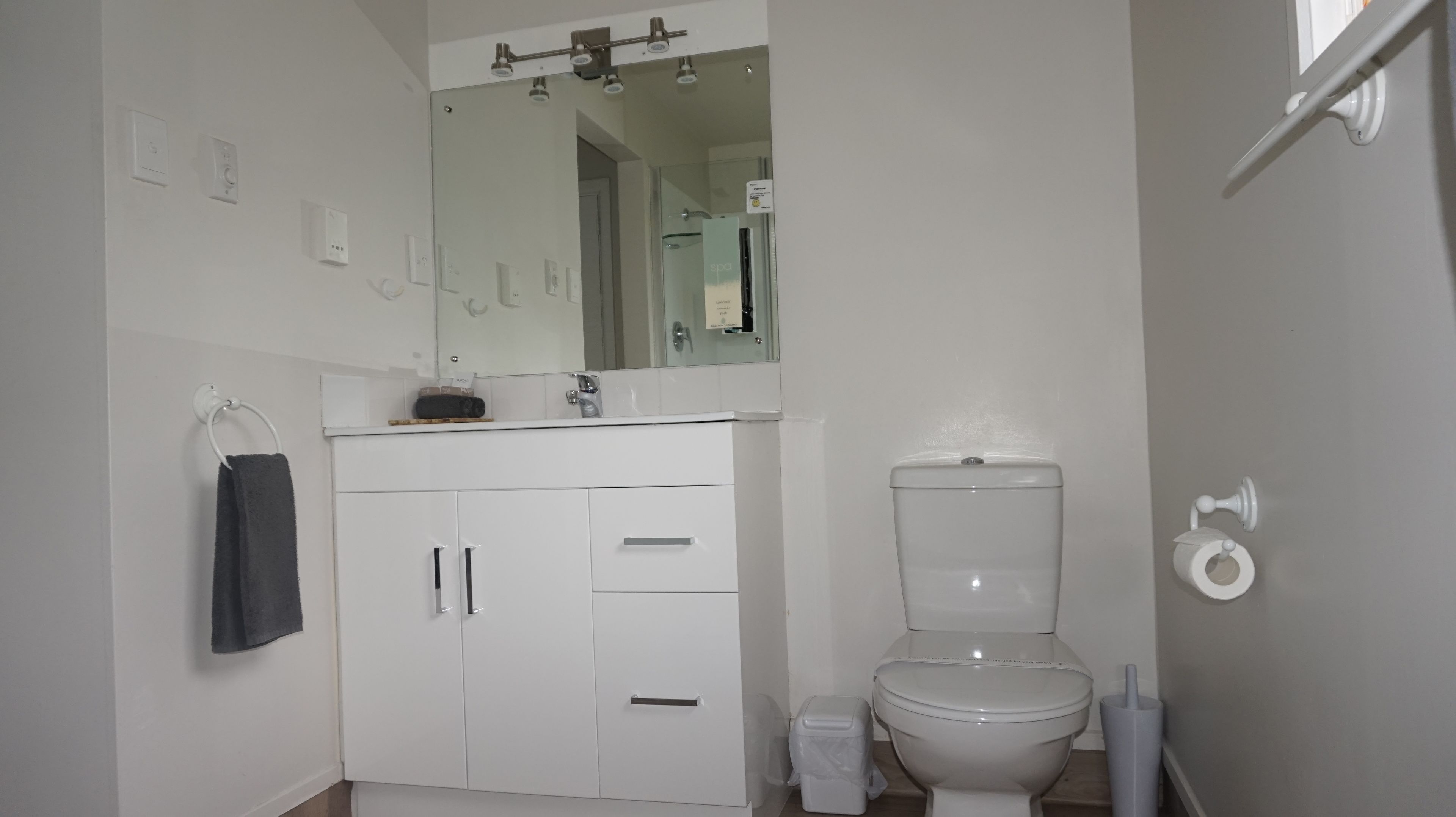 Een moderne badkamer met een wit toilet, een wastafel met spiegel erboven en een handdoek aan een rek.