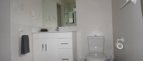 Un baño moderno con un inodoro blanco, un lavabo con un espejo encima y una toalla colgada en un perchero.