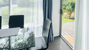 A room with a glass door leading to a garden, a table with chairs, and a view of the outdoors. - Ashleigh Court Motel-Christchurch Hagley Park (Christchurch)